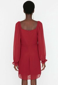 Rotes Kleid mit quadratischem Ausschnitt und langen, puffartigen Ärmeln. Hergestellt aus leichtem Stoff, verfügt es über einen Reißverschluss im Rücken und rüsche Akzente an den Ärmeln.