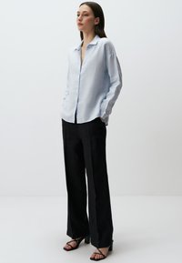 Lichtblauwe, langemouwen overhemd van linnen met een ontspannen pasvorm, gecombineerd met hoge zwarte broek en zwarte sandaaltjes met bandjes.