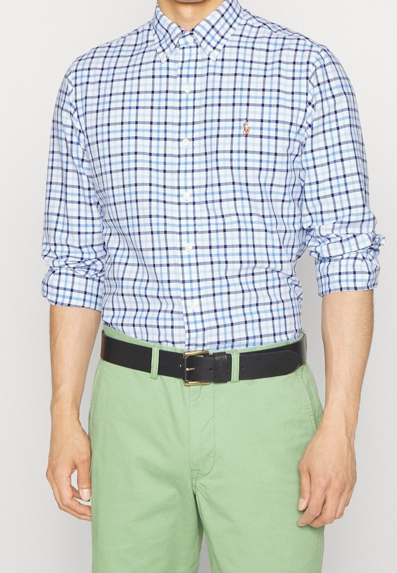 Knappad rutig skjorta i ljusblått och marinblått, med krage, långärmar uppkavlade, i kombination med gröna chinos och ett svart bälte.
