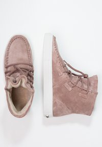 Stivaletti alla caviglia in suede rosa con suola in gomma bianca, caratterizzati da dettagli cuciti e una morbida fodera interna. Lacci fissati attraverso fori decorativi.