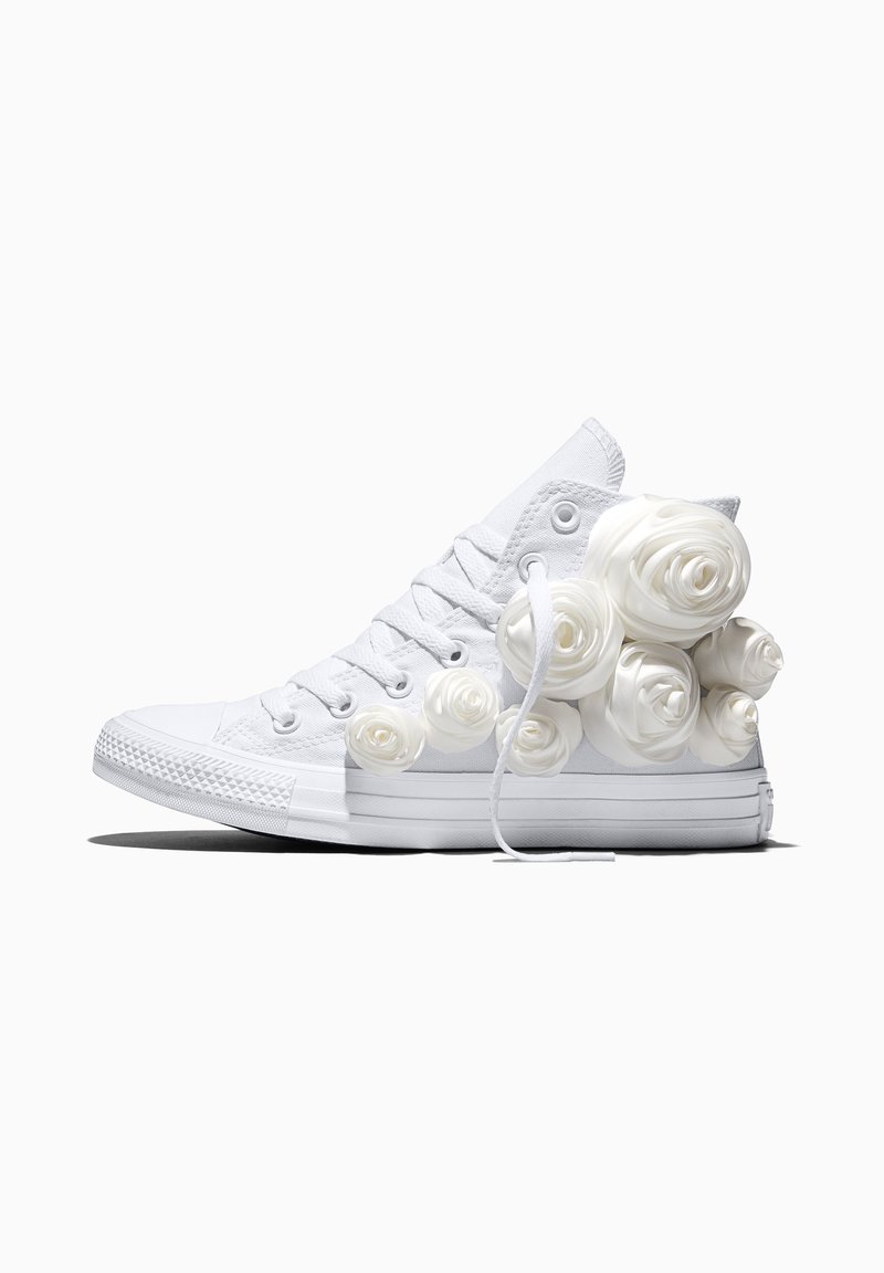 Witte hoge sneaker met wit rozenvormig decoraties bevestigd aan de buitenkant, geplaatst tegen een effen witte achtergrond.