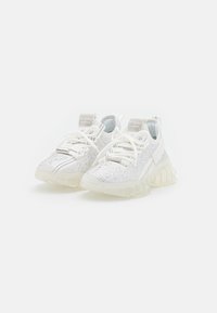 Baskets blanches avec un upper texturé et étincelant, présentant une semelle translucide et des lacets blancs. Comprend une languette texturée au talon.