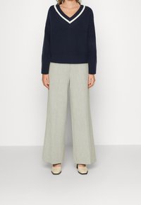 Námořnický pletený svetr s bílým výstřihem do V, zkombinovaný se světle šedými kalhotami se širokými nohavicemi a béžovými botami na blokovém podpatku.