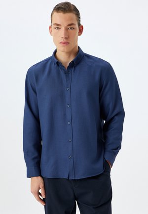 Camisa azul marino de botones con mangas largas, cuello, tejido texturizado y botones a juego, combinada con pantalones oscuros.