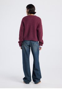 Burgundy fuzzy sweater with a loose fit, ribbed texture, and dropped shoulders. Paired with high-waisted, wide-leg blue jeans.