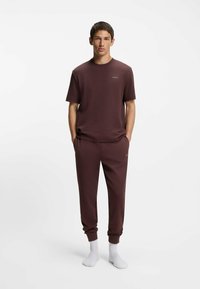 Chemise en tricot bordeaux à manches courtes et pantalon de survêtement assorti avec poignets côtelés, présentant un logo discret, portée avec des chaussettes blanches aux chevilles.