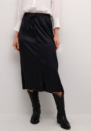 Zwarte satijnen midi-rok met een trekkoord in de taille, een zijslit en een gladde textuur, gecombineerd met zwarte cowboylaarzen met textuuraccenten.