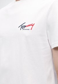 Λευκό βαμβακερό t-shirt με μικρό λογότυπο Tommy Jeans σε ναυτικό μπλε και κόκκινο στην πάνω αριστερή πλευρά του στήθους.