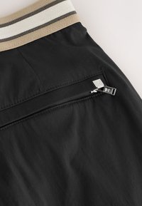 Svarta shorts med en strukturerad midjeresår med beiga och svarta ränder. Inkluderar en liten ficka med dragkedja och silverfärgade detaljer.