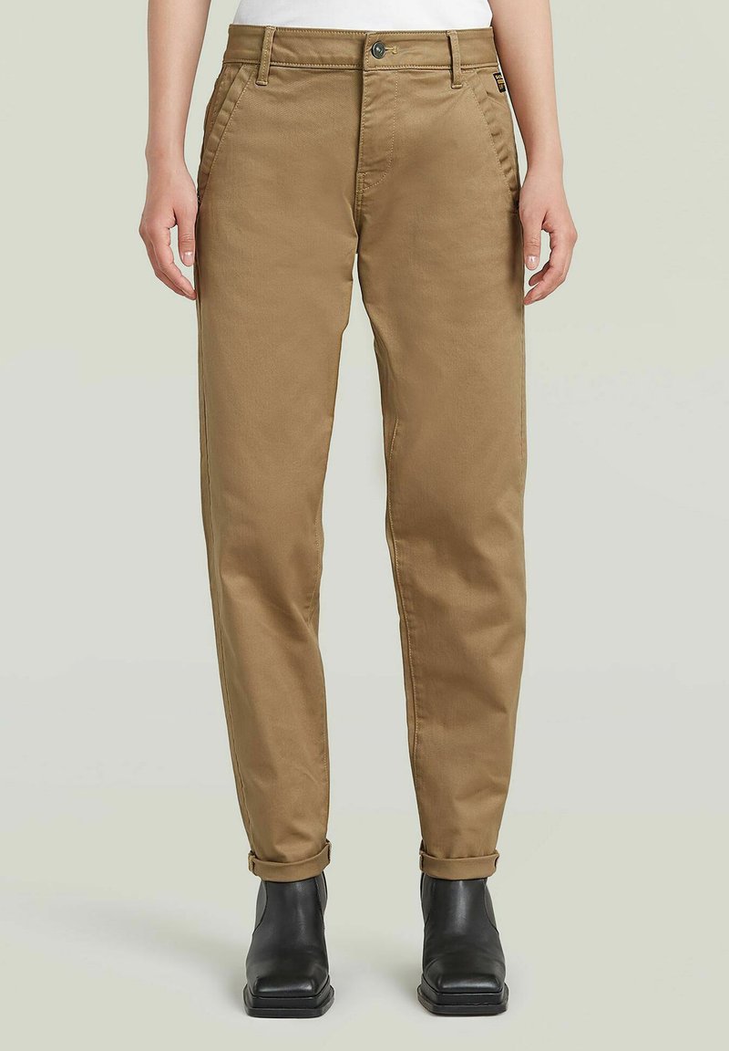 Pantalons en coton beige à coupe droite, avec des ourlets roulés et des poches latérales, assortis à des bottines noires. Design minimaliste avec une coupe classique.