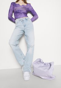 Fialový top s dlouhým rukávem a kulatým výstřihem, světle modré rovné džíny a světle fialová kabelka vedle bílých tenisek.