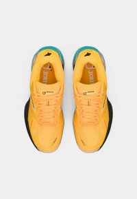 Gelbe Sportschuhe mit strukturiertem Obermaterial, schwarzer Sohle, türkisfarbenen Akzenten und orangenen Schnürsenkeln. Joma-Logo auf der Zunge sichtbar.