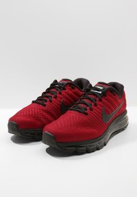 Červené tenisky Nike s síťovaným svrškem, černými akcenty a texturovanou podrážkou. Obsahují šňůrky a polstrovanou mezipodešev pro podporu.