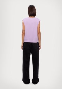 Top lavorato a maglia color lilla con maniche corte e texture a coste, abbinato a pantaloni neri larghi e morbidi, visto da dietro.