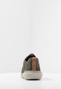 Sneaker verde oliva con tomaia in rete testurizzata, suola in gomma beige e linguetta in pelle sul tallone. Presenta un accento bianco cucito attorno alla suola.
