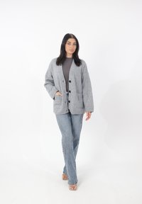 Cardigan grigio lavorato a maglia con vestibilità morbida, due tasche frontali e chiusura con bottoni. Abbinato a jeans di denim chiaro e sandali aperti.