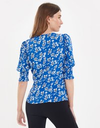 Blusa floreale blu con maniche a palloncino, polsini elastici e design aderente. Il tessuto ha una texture liscia con motivi di fiori bianchi e neri.