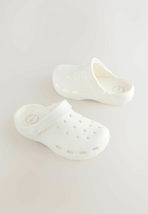 Beli leseni natikači iz lahkega materiala z zaprtim prstom, odprtim hrbtom, luknjicami za prezračevanje in kontrastnim trakom za varno prileganje.