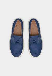 Ζευγάρι μπλε σουέντ μοκασίνια με κορδόνια και λευκές λαστιχένιες σόλες, σε άποψη από πάνω, σε λευκό φόντο.