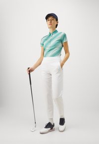 Golf apģērbs, kas sastāv no zaļi un balti svītrainā polo krekla, baltiem biksēm un melnbaltiem golfam paredzētiem apaviem. Aksesuārs ir melns golfa nūja.