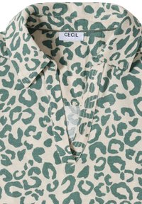 Chemise à col avec motif léopard vert sur tissu beige et une étiquette "CECIL" à l'encolure.