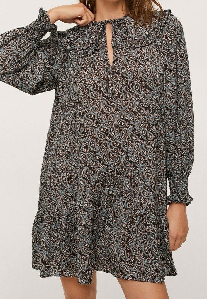 Femme portant une robe longue à manches longues, longueur genou, avec des motifs cachemire bleus et bruns, ainsi que des poignets et un col à volants.