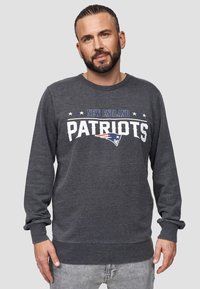 Sudadera gris con el texto "New England Patriots" en blanco y azul, de mangas largas, con puños y dobladillo acanalados, fabricada en un tejido suave.