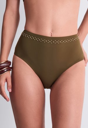 Femme portant un bas de bikini taille haute vert olive avec de petits clous dorés le long de la ceinture et des bracelets en bois au poignet gauche.