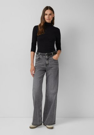 Zwarte coltrui met aansluitende mouwen; grijze high-waisted, wijde jeans met riem; neutraal gekleurde schoenen met een gestructureerde zool; effen achtergrond.