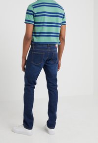 Blå denimjeans med slim fit, med bakfickor och kontrasterande sömmar. I kombination med en grön och blå randig T-shirt och vita sneakers.