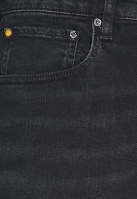 Tmavě modré džíny s klasickým pětipocket designem, malou kapsou vepředu, měděnými a stříbrnými nýtovými detaily a hladkou texturou.