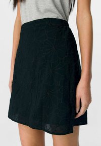 Falda negra bordada con patrón floral, tejido ligero, forma evasé, apertura lateral y detalles de textura sutiles.