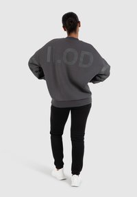 Felpa oversize grigia scura con la scritta "ILOD" stampata sul retro; abbinata a pantaloni neri slim-fit e sneakers bianche. Tessuto liscio.