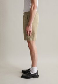 Beige cotton shorts with an elastic waistband, side pockets, and a straight cut. Paired with black loafers and white socks.