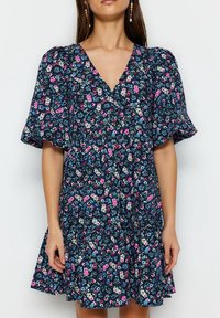Kwiatowa sukienka na ciemnoniebieskim tle, krótki bufiaste rękawy, dekolt w kształcie litery V i rozkloszowany dół. Posiada różowe, białe i turkusowe kwiaty w całej kompozycji.