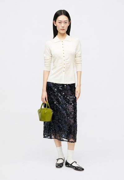 White long-sleeve button-up top, sequined black skirt, green handbag, white socks, and black Mary Jane shoes with white accents.