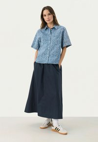 Hellblaues, blumengemustertes Kurzarmhemd mit Kragen, kombiniert mit einem langen, dunkelblauen Rock und weißen Sneakers mit schwarzen Streifen.