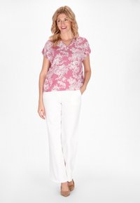 Blusa floreale rosa con maniche corte e scollatura a V, abbinata a pantaloni bianchi a gamba larga e tacchi beige. Tessuto dalla superficie liscia.