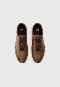 Brune lærersneakers med rund tå og kontrasterende kremgummisåle. Har mørkebrune snører og merke på tungen. Smooth tekstur.