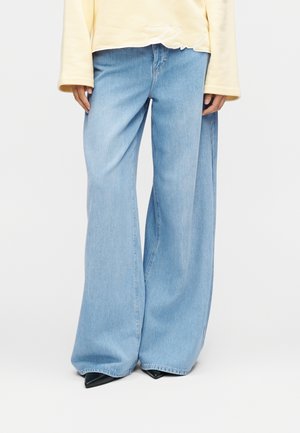 Jeans larges bleu clair en denim, à taille haute et légèrement usés à l'ourlet, associés à des chaussures noires à bout pointu.