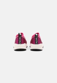 Zapatillas de deporte rosas con purpurina y un acabado texturizado, que incluyen una cinta de agarre negra marcada con "TWINS" y suelas blancas. Forma redondeada con bordes suaves.