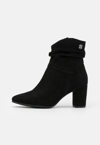 Bota de tobillo de ante negra con puño arrugado, punta afilada y tacón cuadrado. Presenta un pequeño detalle de herraje floral plateado.