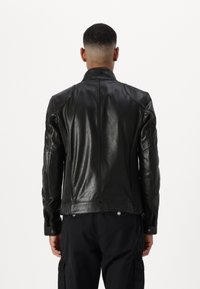 Veste en cuir noir avec un col haut, un design ajusté et une texture côtelée sur les côtés. Comprend des boutons-pression et une finition lisse.