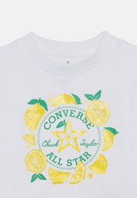 Λευκό t-shirt με γραφικό σχέδιο κίτρινων λεμονιών και πράσινων φύλλων γύρω από έναν κυκλικό λογότυπο "Converse Chuck Taylor All Star".