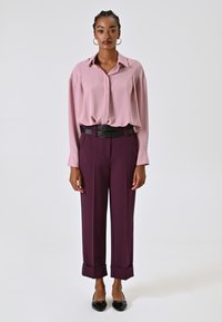 Blouse rose clair à manches longues avec un col, assortie à un pantalon taille haute violet foncé avec ourlets retroussés et une ceinture double noire.