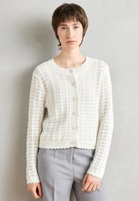 Weißer Strickcardigan mit einem strukturierten Zickzackmuster, gerippten Bündchen und einem gewellten Halsausschnitt. Verfügt über fünf Knöpfe auf der Vorderseite.