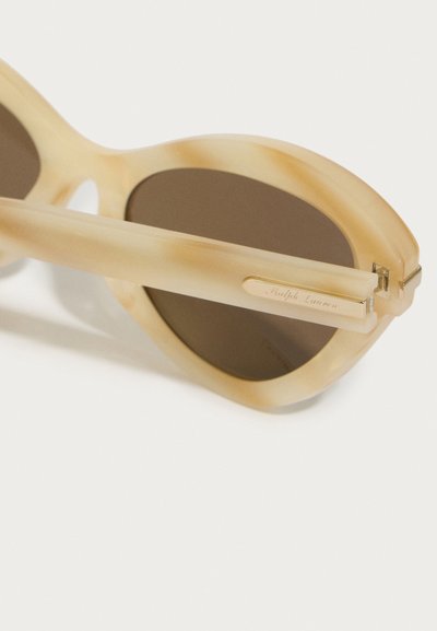 Beige sluneční brýle s charakteristickým tvarováním kočičích očí, transparentním rámem, hnědými skly a stříbrnými detaily s nápisem "Ralph Lauren."
