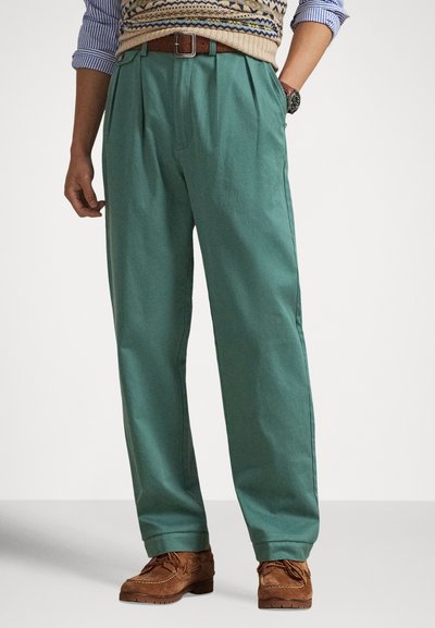 Zielone plisowane spodnie bawełniane o luźnym kroju, z bocznymi kieszeniami i paskiem na talii z brązowej skóry.