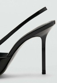 Crne sandale na visokoj potpetici s sjajnom površinom, tankim remenom i suženim potplatom. Imaju elegantan, šiljast nos i vitku potpeticu.