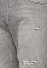 Jeans de mezclilla gris con detalles desgastados, incluyendo roturas y bordes deshilachados. Textura suave con sutiles acentos de costura.